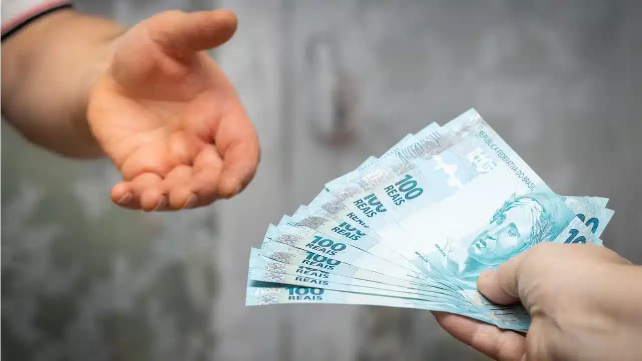 Pessoa entregando várias notas de R$ 100 para outra pessoa.