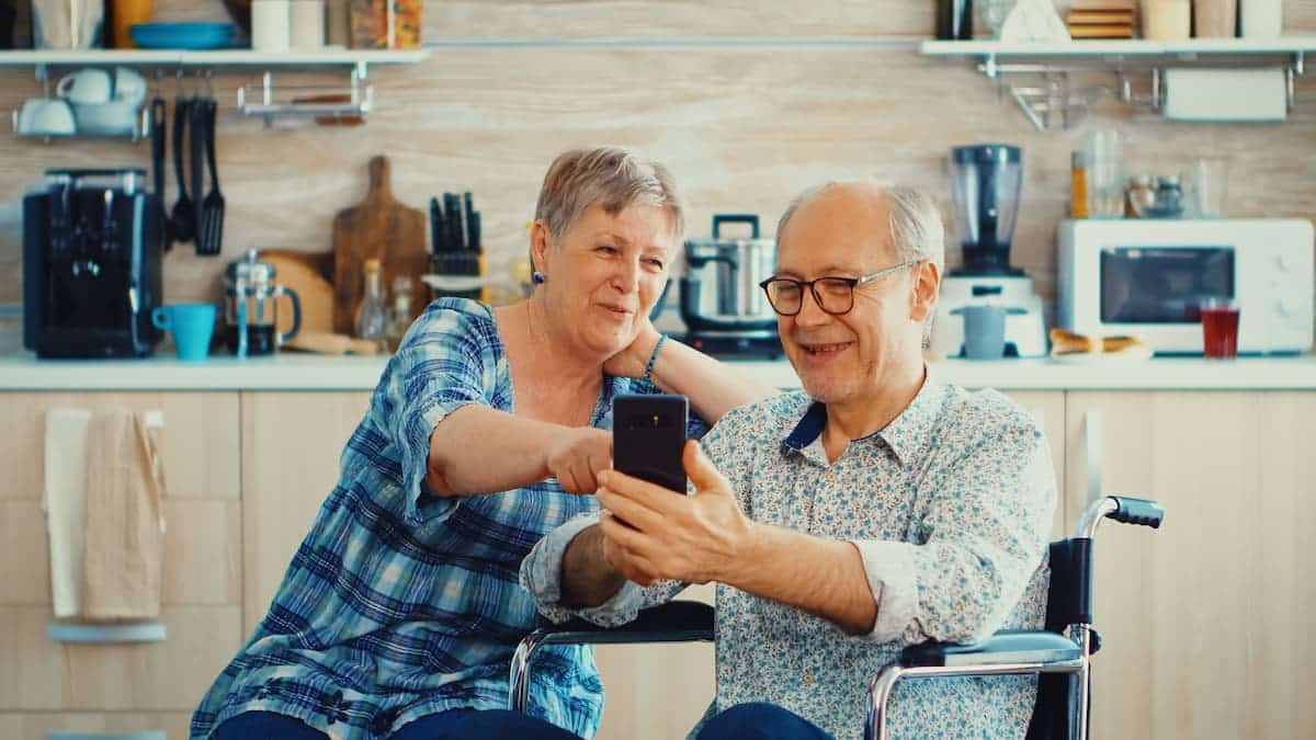 Casal de idosos sorrindo e olhando para um celular. BPC Bolsa Família
