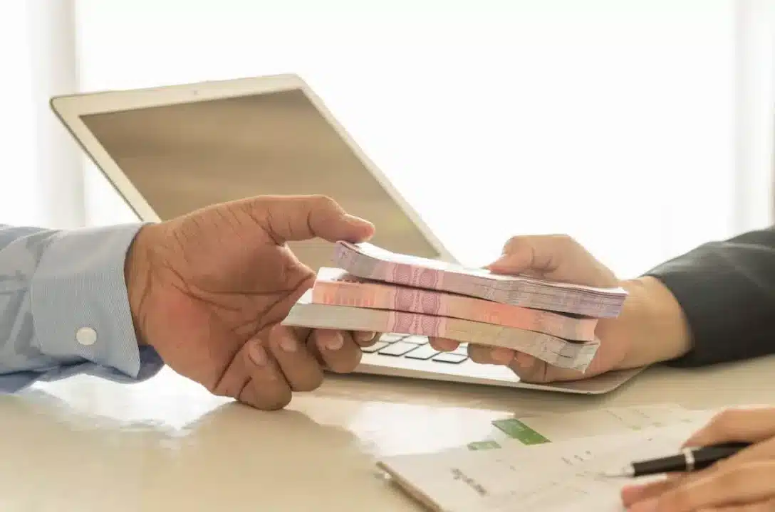 Na imagem, pessoa recebendo maço de dinheiro de outra depois de conseguir linha de crédito