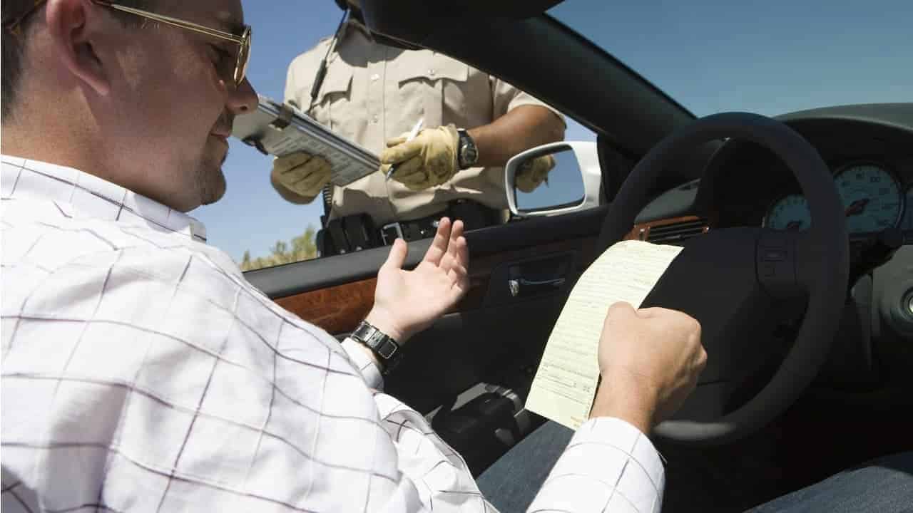 A imagem mostra um condutor recebendo uma multa.