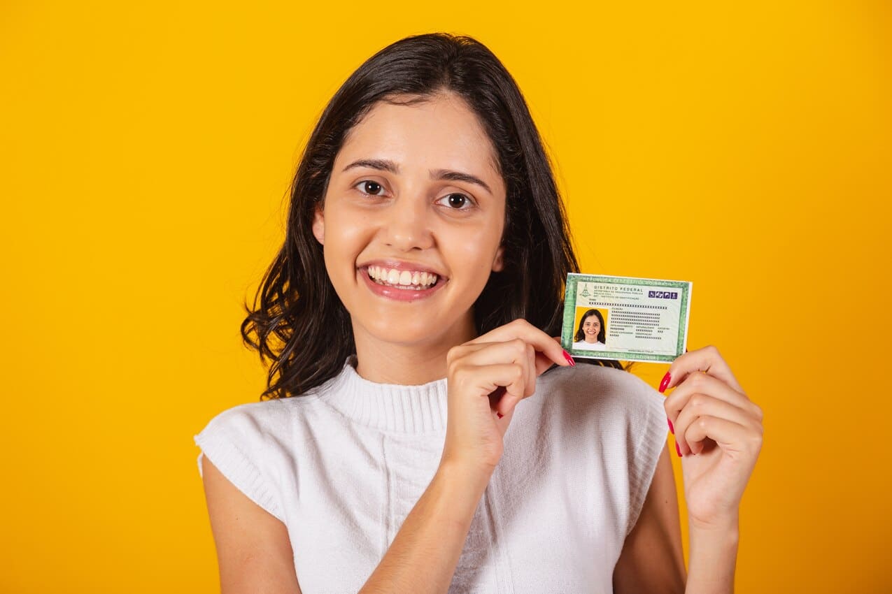 Na imagem, mulher segurando carteira de identidade RG