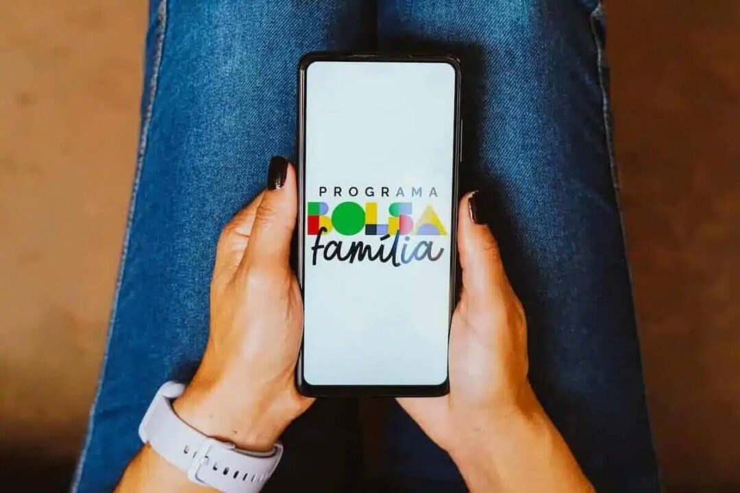 Mãos segurando celular que mostra a logo do Bolsa Família.