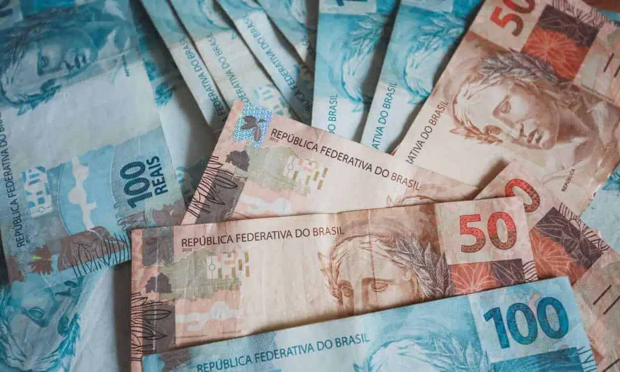 Várias notas de R$100 e R$50 espalhadas sobre uma mesa referente a pagamento