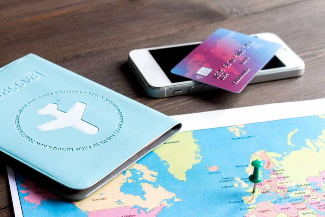 Sobre uma mesa, um mapa de viagem, uma miniatura de avião, um celular e um cartão de crédito.