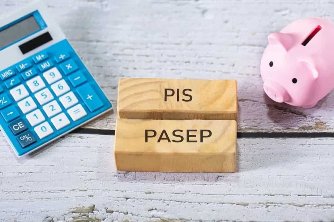 Blocos de madeira escrito "PIS" e "PASEP". Ao lado direito do bloco tem uma calculadora azul e do lado esquerdo um cofrinho de porco rosa.