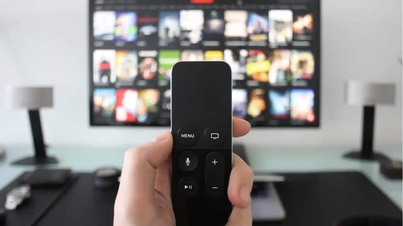 Mão segurando controle remoto na frente de TV.