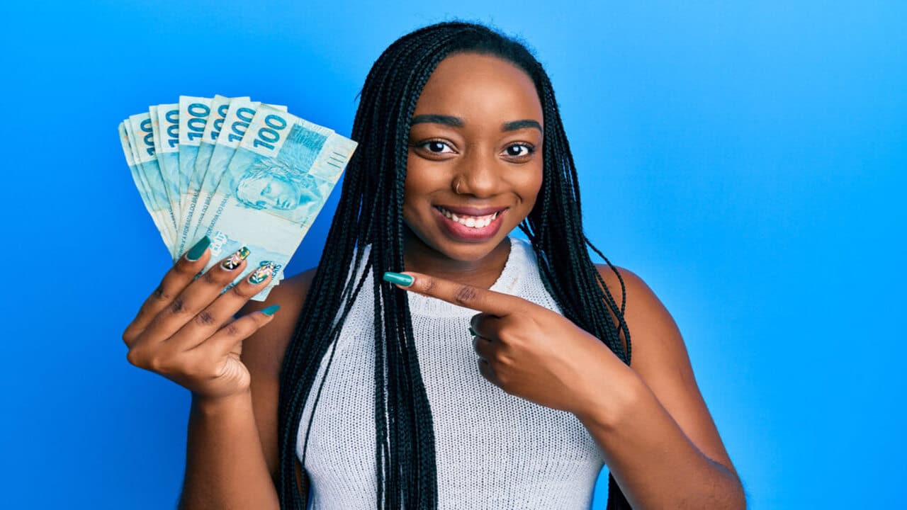 mulher negra segurando notas de dinheiro após aumento R$ 300 abono salrial