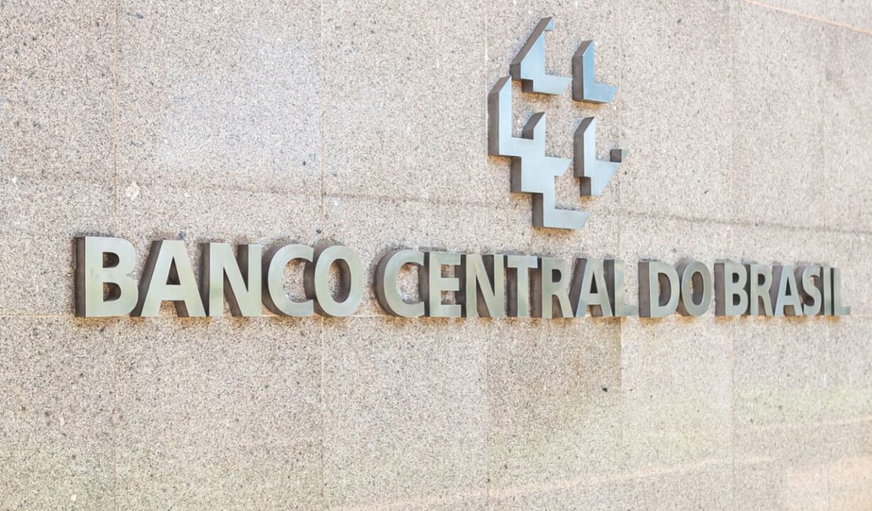 fachada do Bancos Central do Brasil, com letras e logotopo metálicos na cor cinza sobre uma parede de concreto cinza claro
