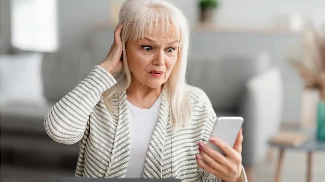 Mulher com expressão de surpresa olhando para um celular idosos