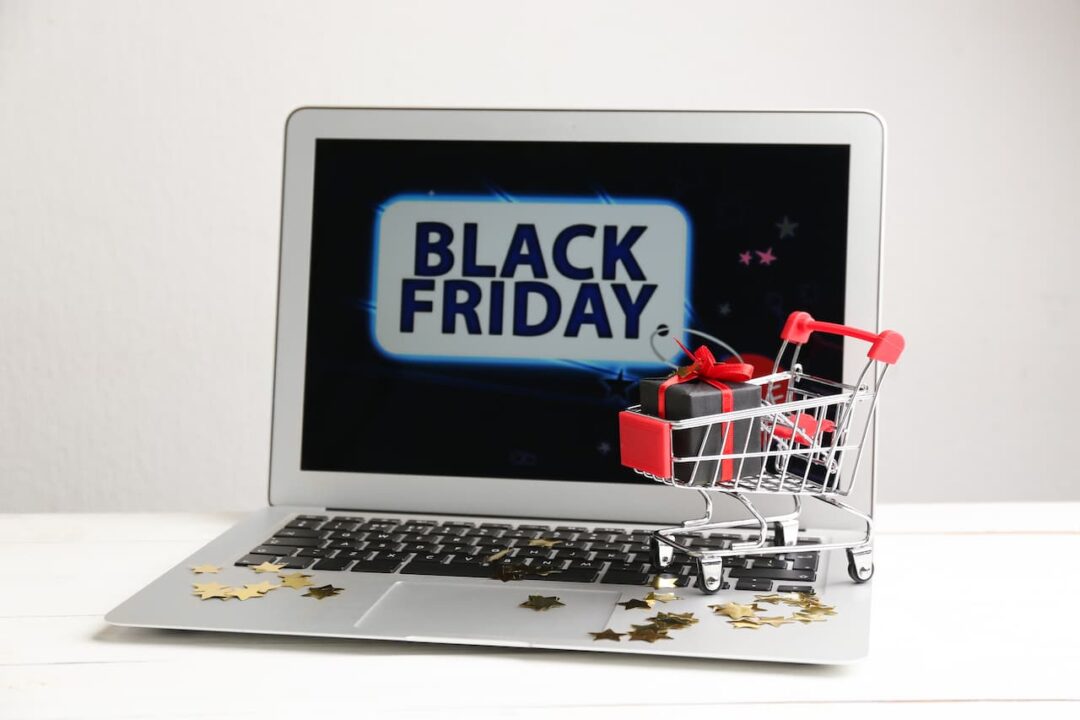 Imagem de um computador com a tela escrito "black friday" e em cima do teclado um mini carrinho de compras com um pacote de presente dentro.