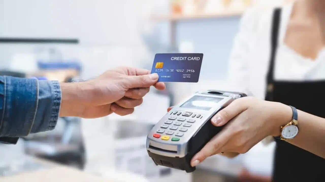 Pessoa segurando cartão de crédito e outra segurando maquininha de cartão