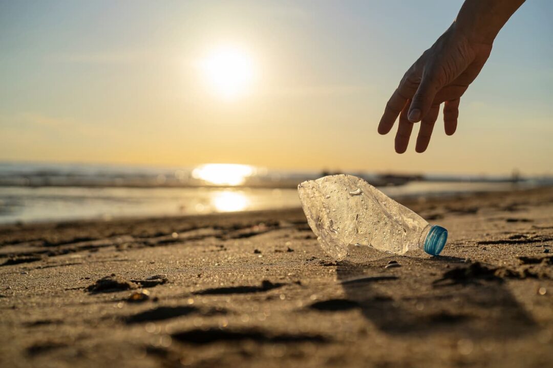 Silhueta de mão pegando garrafa de plástico na praia
