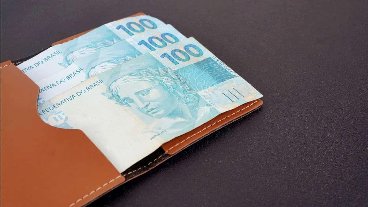 Notas de 100 reais sobre um carteira marrom.