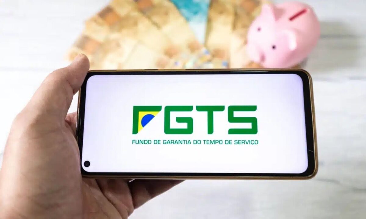 Mão segurando celular com aplicativo do FGTS na tela inicial.