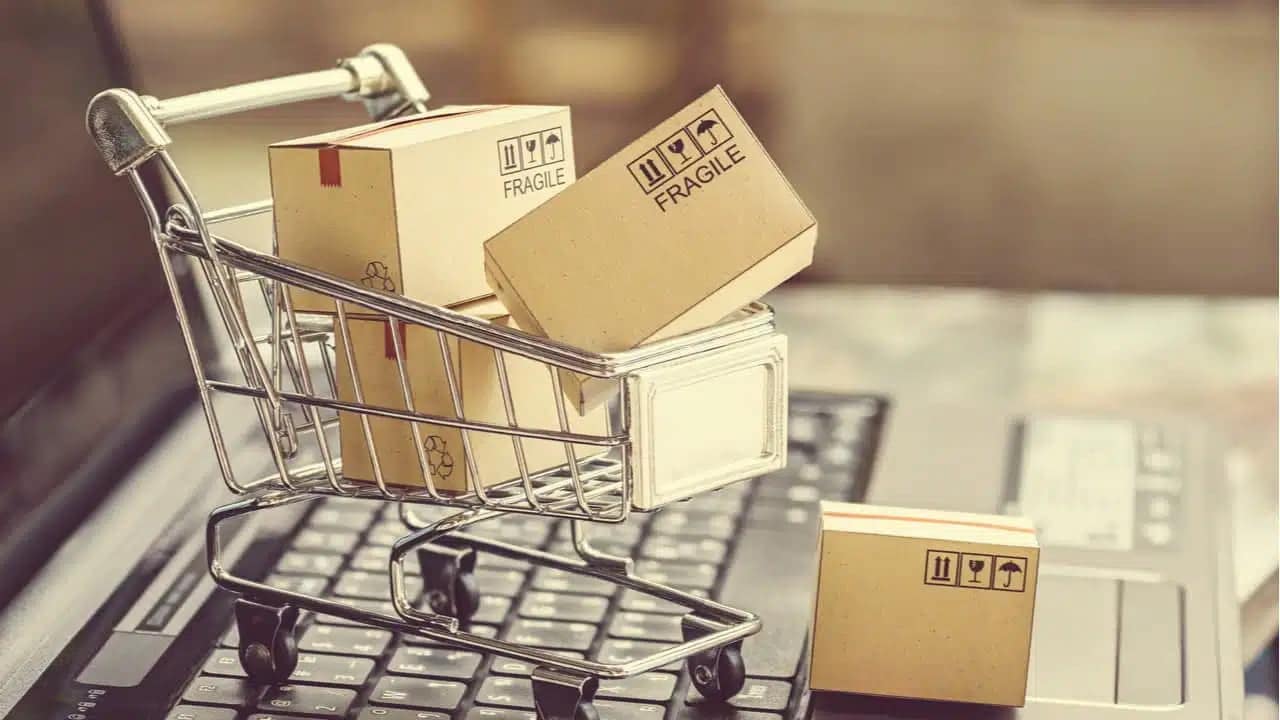 Em cima de um teclado, miniatura de carrinho de compras com pequenas caixas de papelão