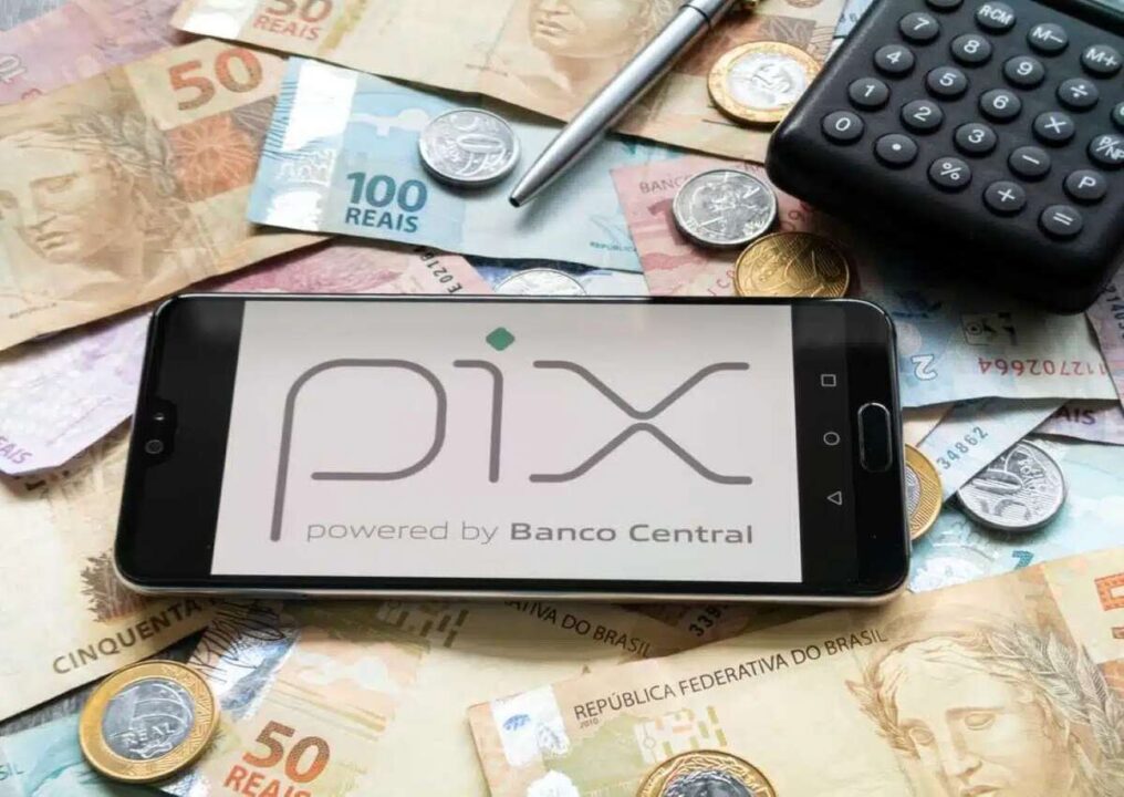 Celular com o nome PIX na tela inicial, sobre algumas cédulas de dinheiro e moedas.