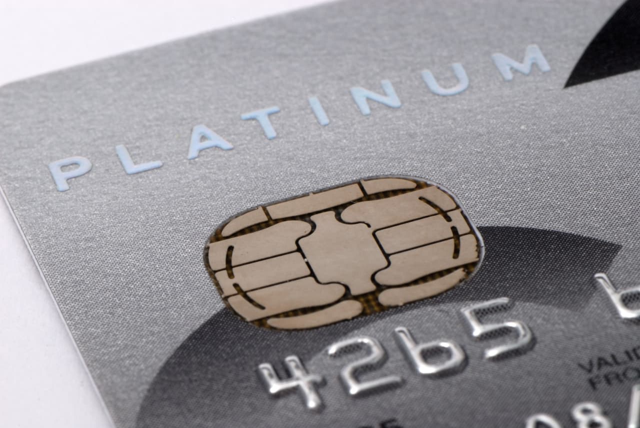 Detalhe do canto de um cartão de crédito na cor cinza, revelando a palavra “platinum” e mostrando o chip do objeto.
