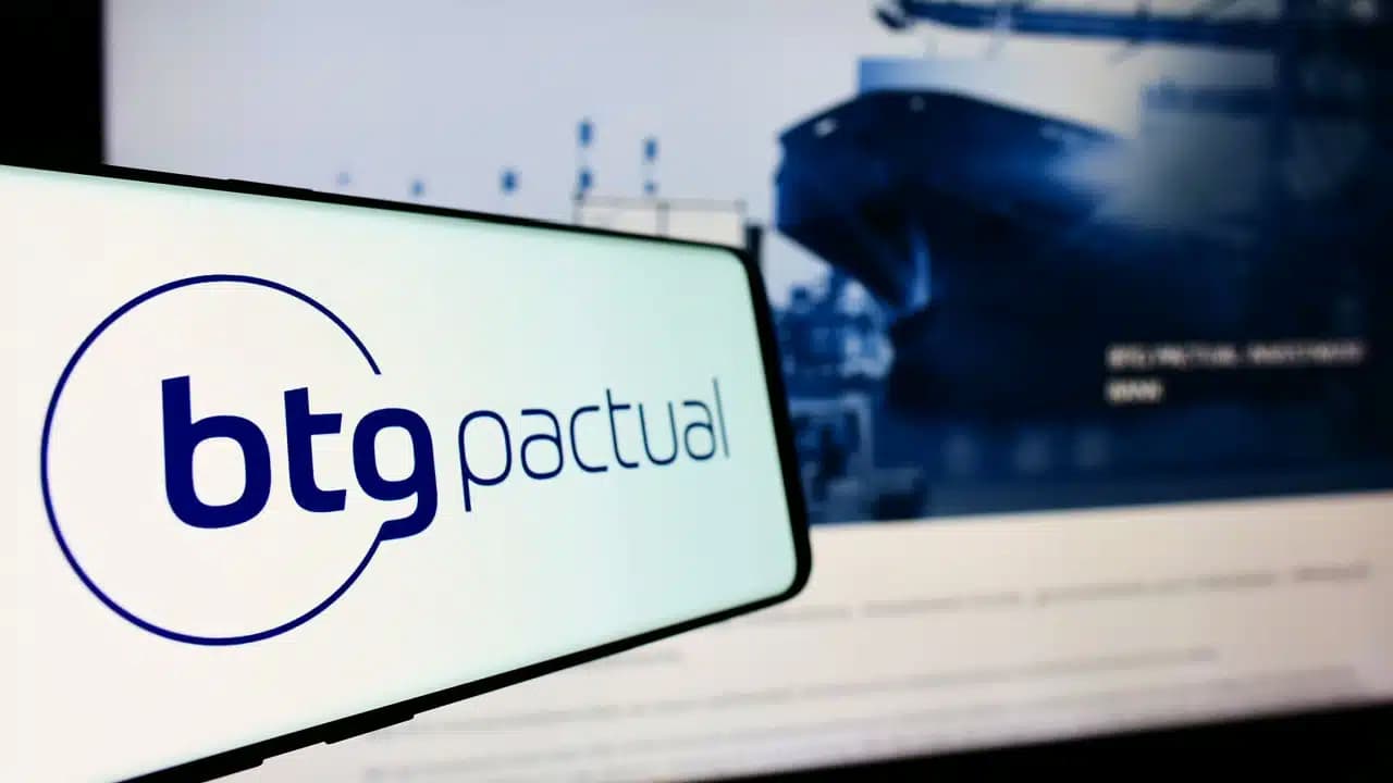 Celular na horizontal mostrando logo do banco BTG Pactual. Ao fundo, tela mostrando site da empresa.