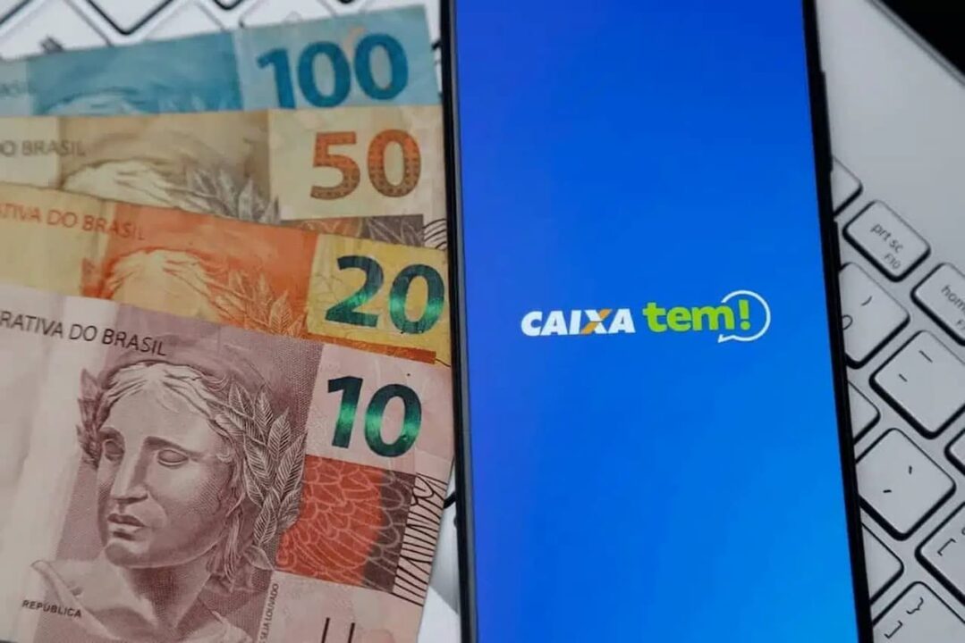 Celular com app Caixa Tem e várias notas de dinheiro ao lado