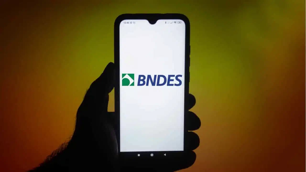 Mão segurando celular com logo do BNDES