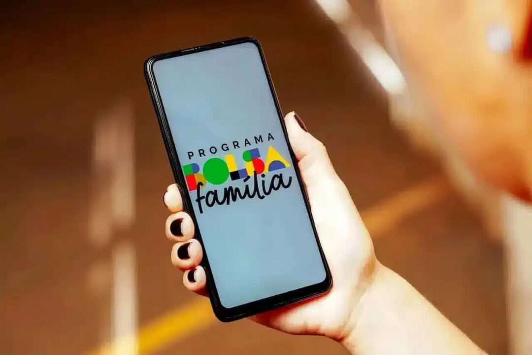 Mão segurando celular com tela mostrando nome do programa Bolsa Família