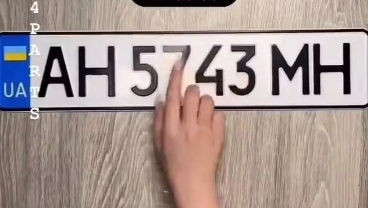 Pessoa colando adesivo anti-radar em uma placa de carro,