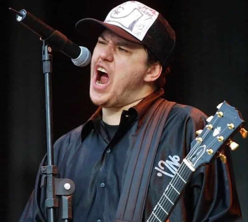 Imagem de Chorão, de boné cantando em uma microfone e uma guitarra