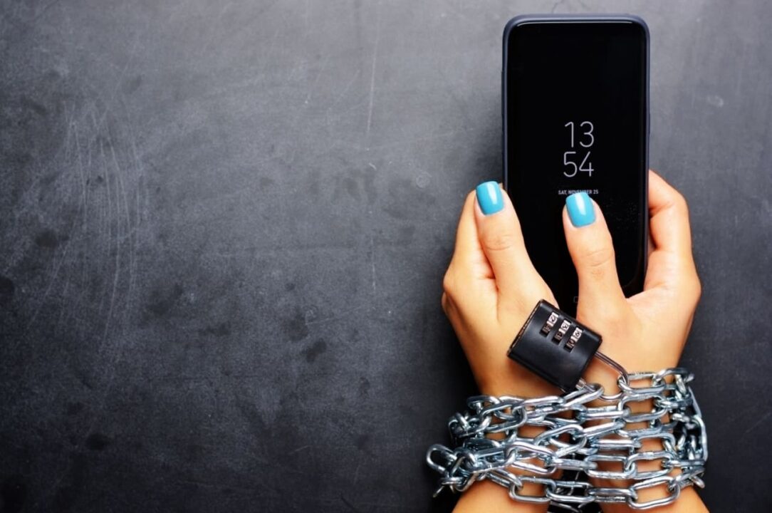 Mãos presas com corrente e cadeado segurando um celular