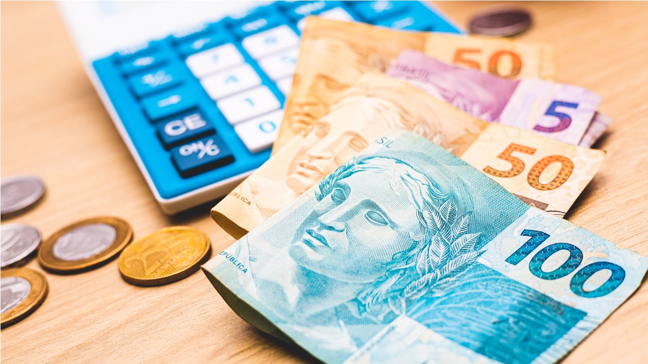 Diversos notas de dinheiro, moedas e uma calculadora sobre mesa