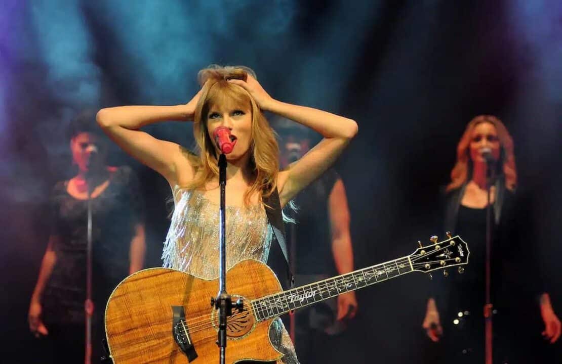 Taylor Swift com as duas mãos no cabelo enquanto canta em show