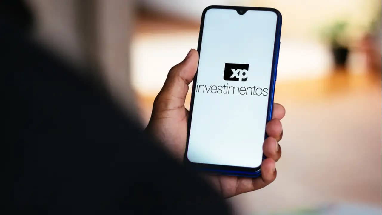 Mão de uma pessoa segurando celular que mostra logo da XP Investimentos