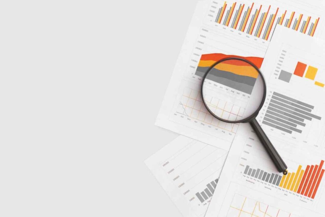 Lupa em cima de folhas com gráficos representando a organização financeira