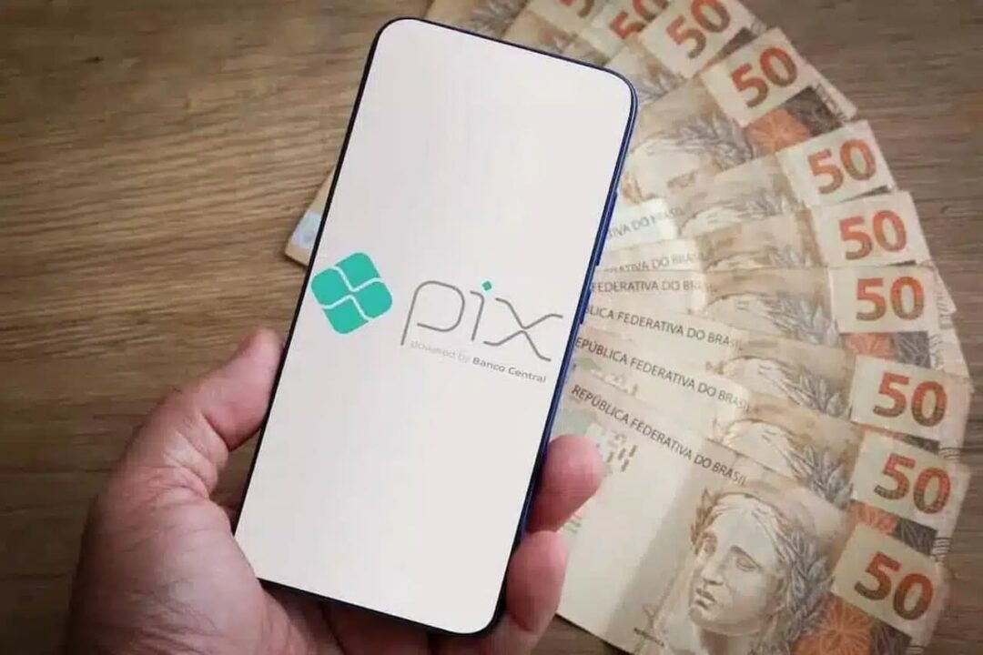 Celular com a logo do Pix na tela e diversas notas de R$ 50,00 ao fundo