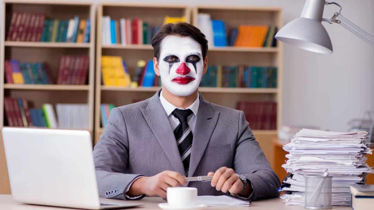 Homem fantasiado de palhaço para o Carnaval e trabalhando em escritório, com expressão desanimada