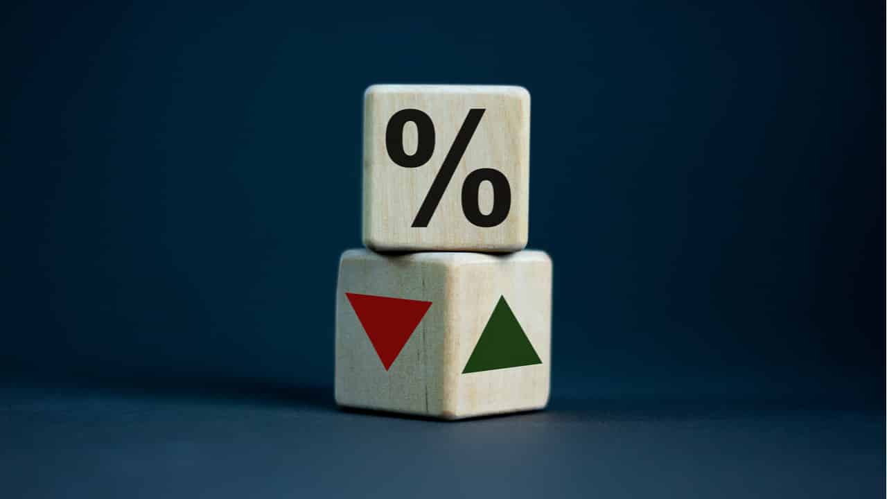 Dois dados, um em cima do outro. Em um, há o símbolo de porcentagem, no outro, uma seta verde indicando para cima e uma seta vermelha indicando para baixo.