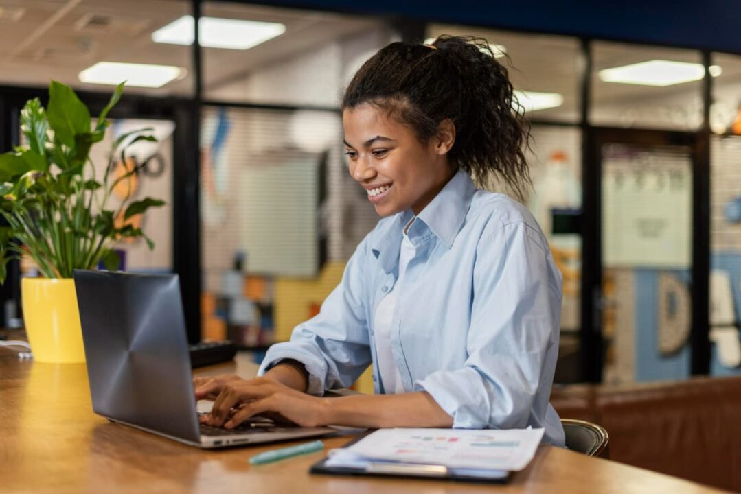 jovem trabalhadora sorrindo enquanto digita em computador