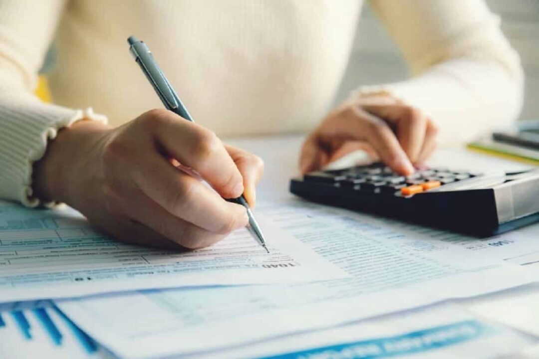 Imagem de uma pessoa realizando cálculos utilizando uma calculadora e caneta Imposto de Renda