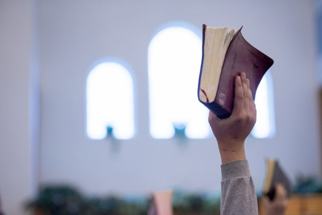 Mão levantada para cima enquanto segura uma bíblia, dentro de uma igreja