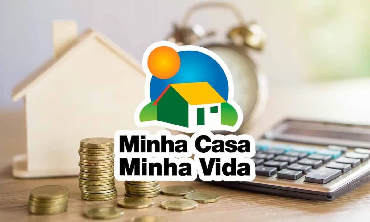 Miniatura de casa, pilha de moedas, despertador e calculadora sobre uma mesa e, em frente, o logo do programa Minha Casa, Minha Vida