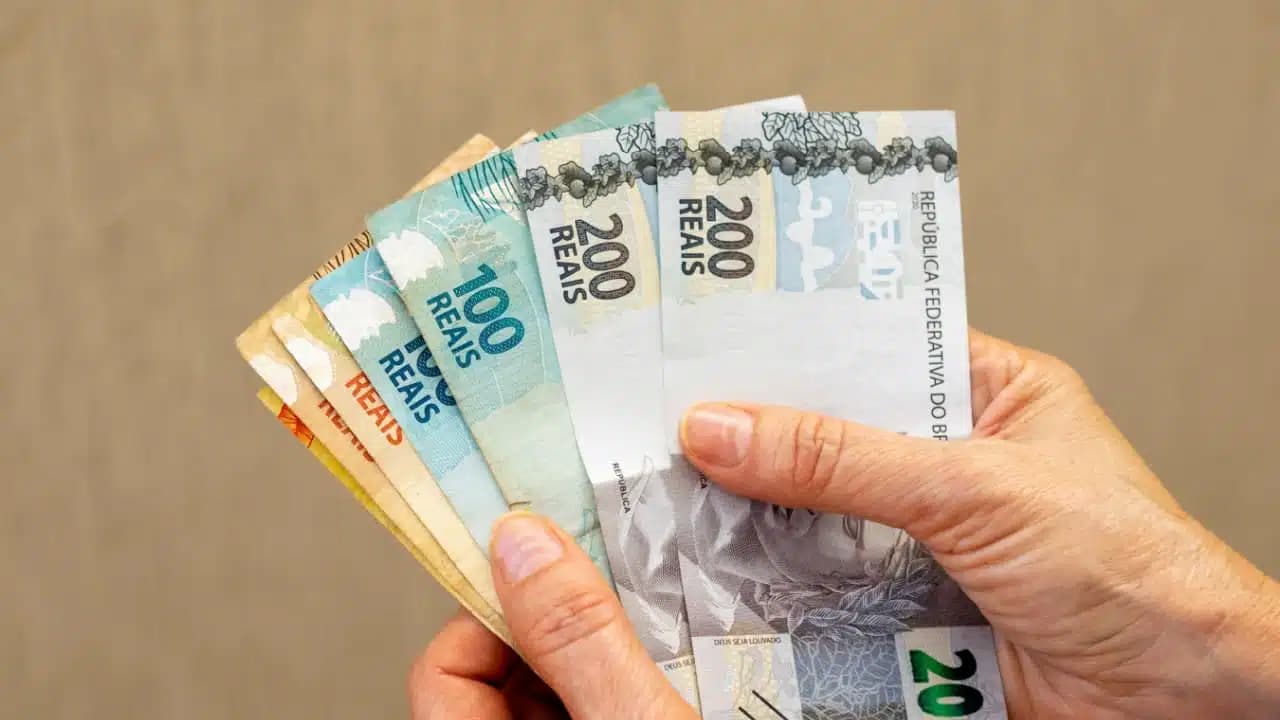 Mão segurando diversas notas de dinheiro referente a salário