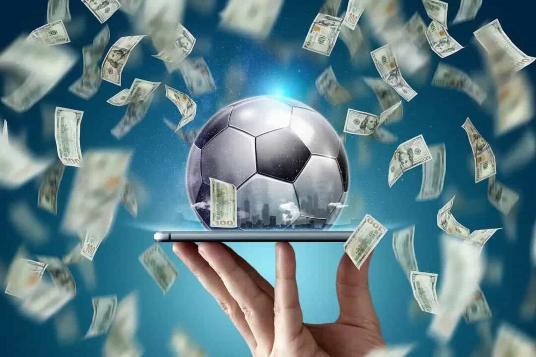 Uma bola em cima de uma tela de celular com notas de dinheiro caindo, representando apostas online.