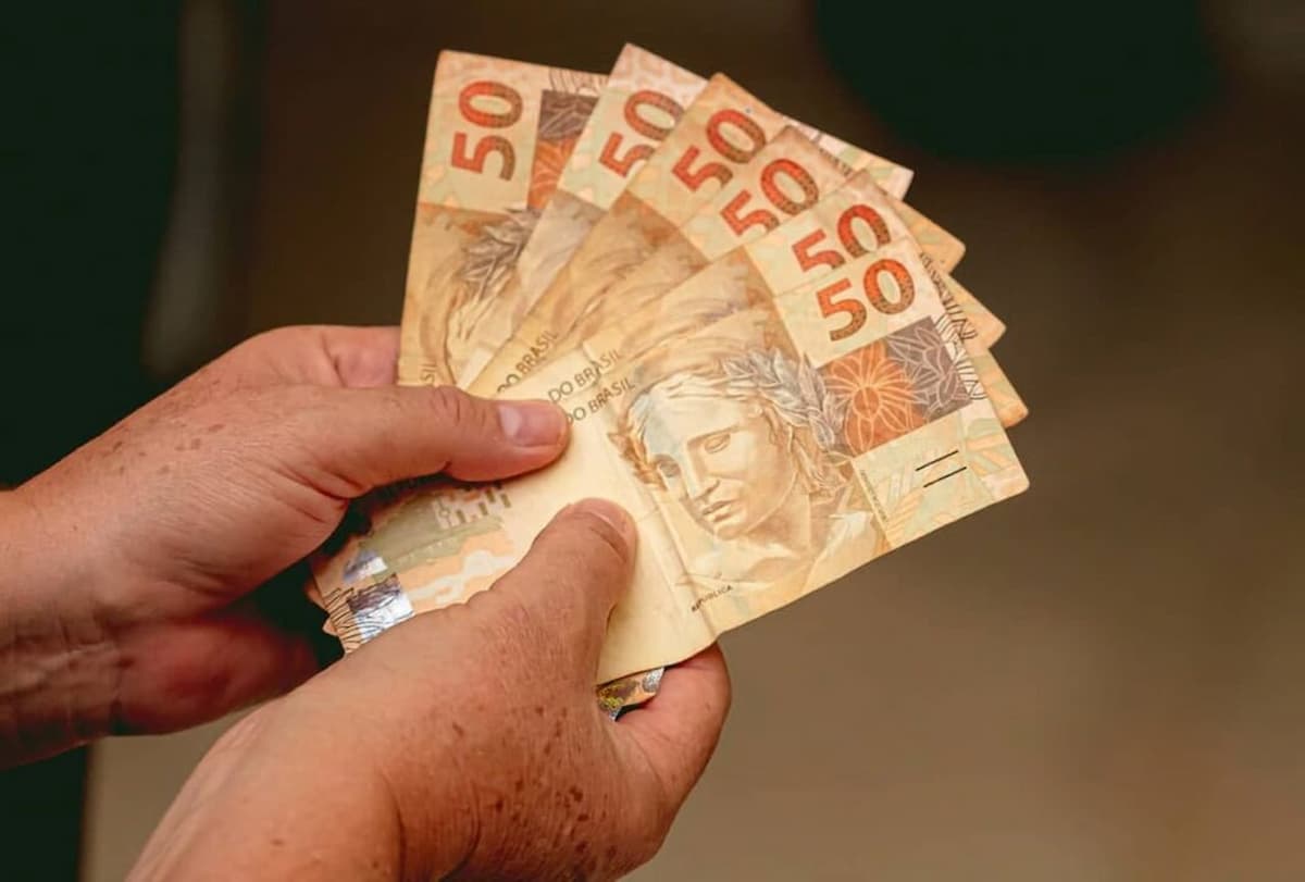 Mãos seguram notas de R$ 50 representando auxílio moradia.