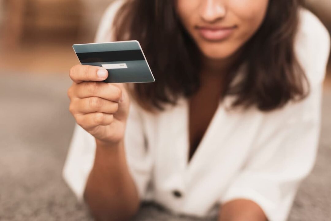 A imagem mostra uma mulher segurando um cartão de crédito e, segundo a expressão dos lábios, pensativa.