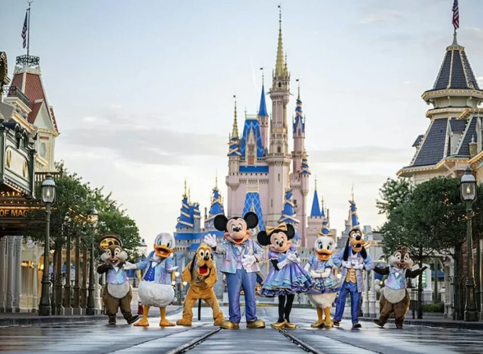 Personagens da Disney (Tico e Teco, Pato Donald, Pluto, Pateta, Mickey Mouse, Minnie Mouse e Margarida) em frente ao castelo do parque