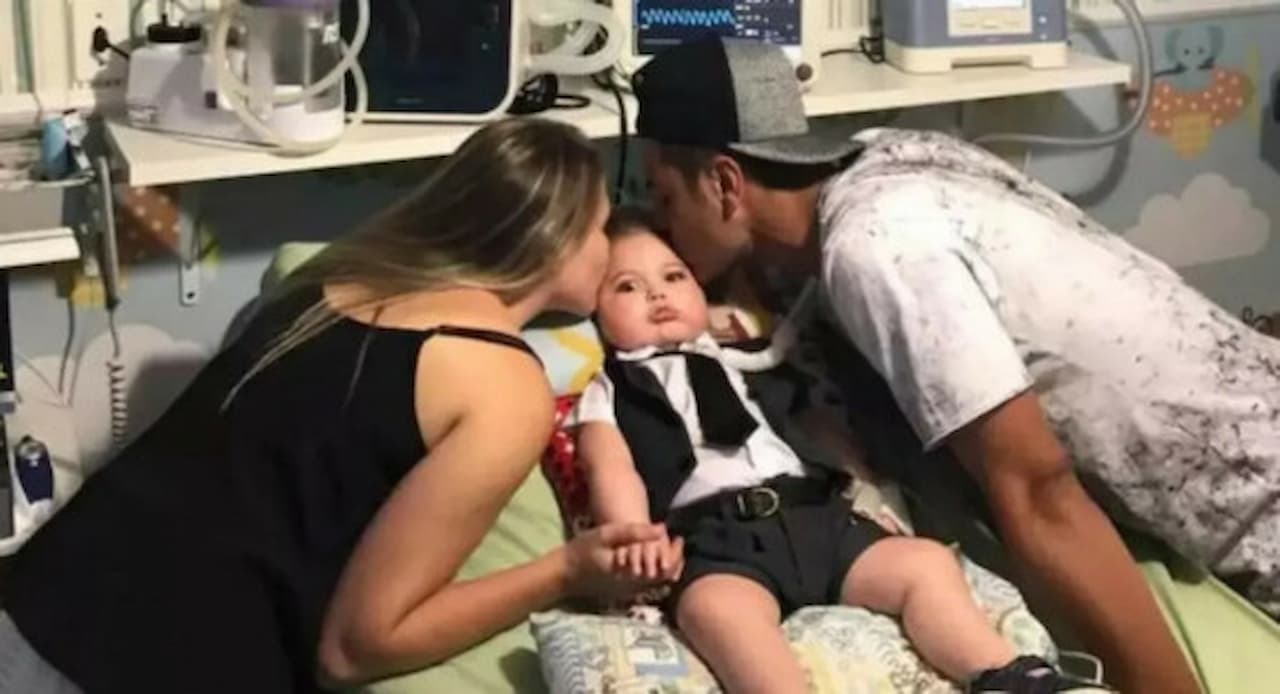 Imagem dois pais beijando o filho em uma cama de hospital