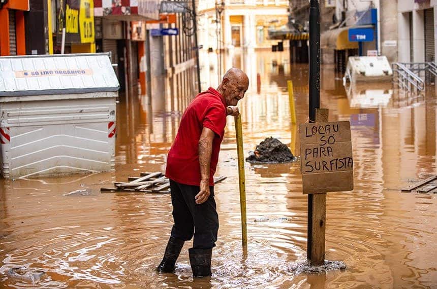 Idoso de botas de chuva em meio à enchente