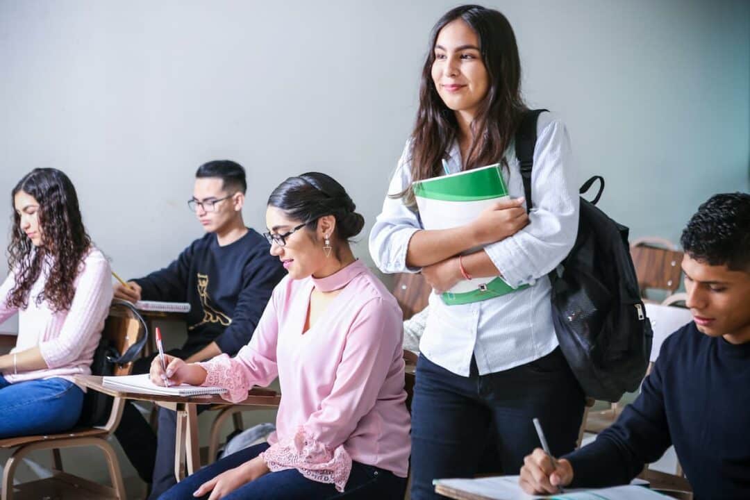 Imagens de jovens sentados em classes. Uma jovem está em pé, com livros nos braços